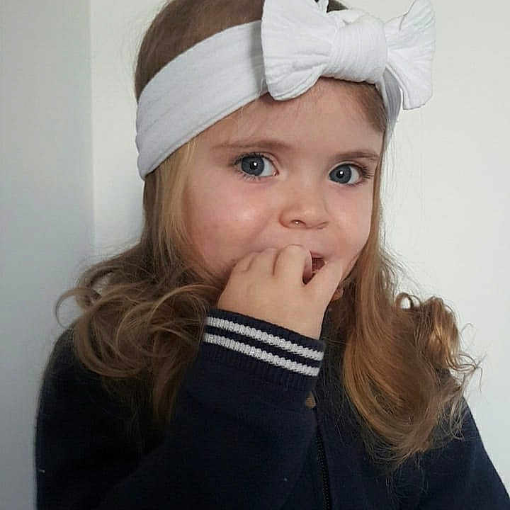 Nelya is registered to the contest to win money with this photo: blue_eyes, casual_clothing, child, curly_hair, cute, expression, face, girl, hand_near_mouth, headband, indoor, light_background, long_hair, looking, person, portrait, sweater, thoughtful, white_bow, young