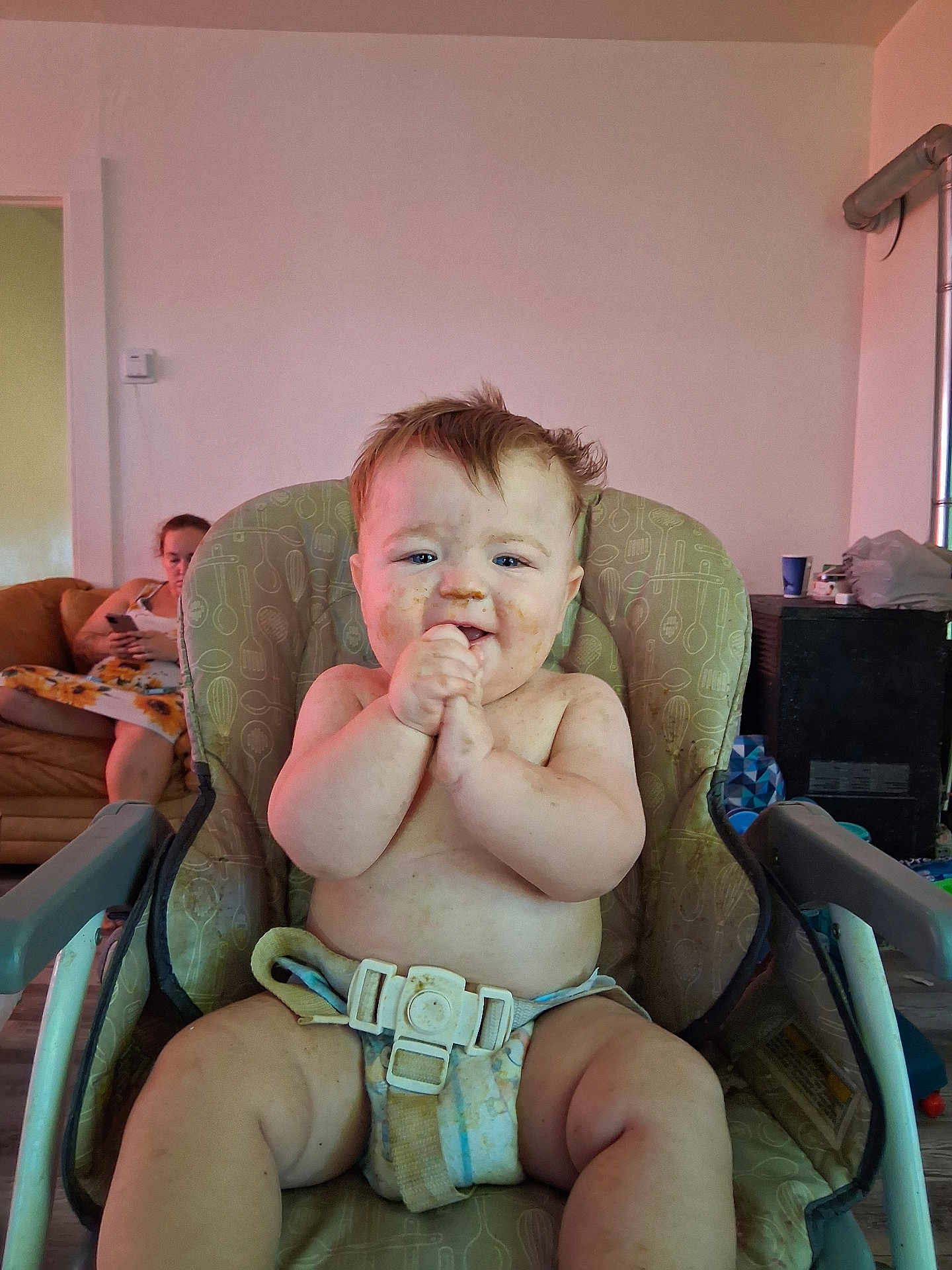 Patrick is registered to the contest to win money with this photo: baby, high_chair, messy, food_smear, clapping, happy, indoor, person, woman, couch, phone, living_room, furniture, diaper, child, smile, seat_belt, home, casual, relaxed