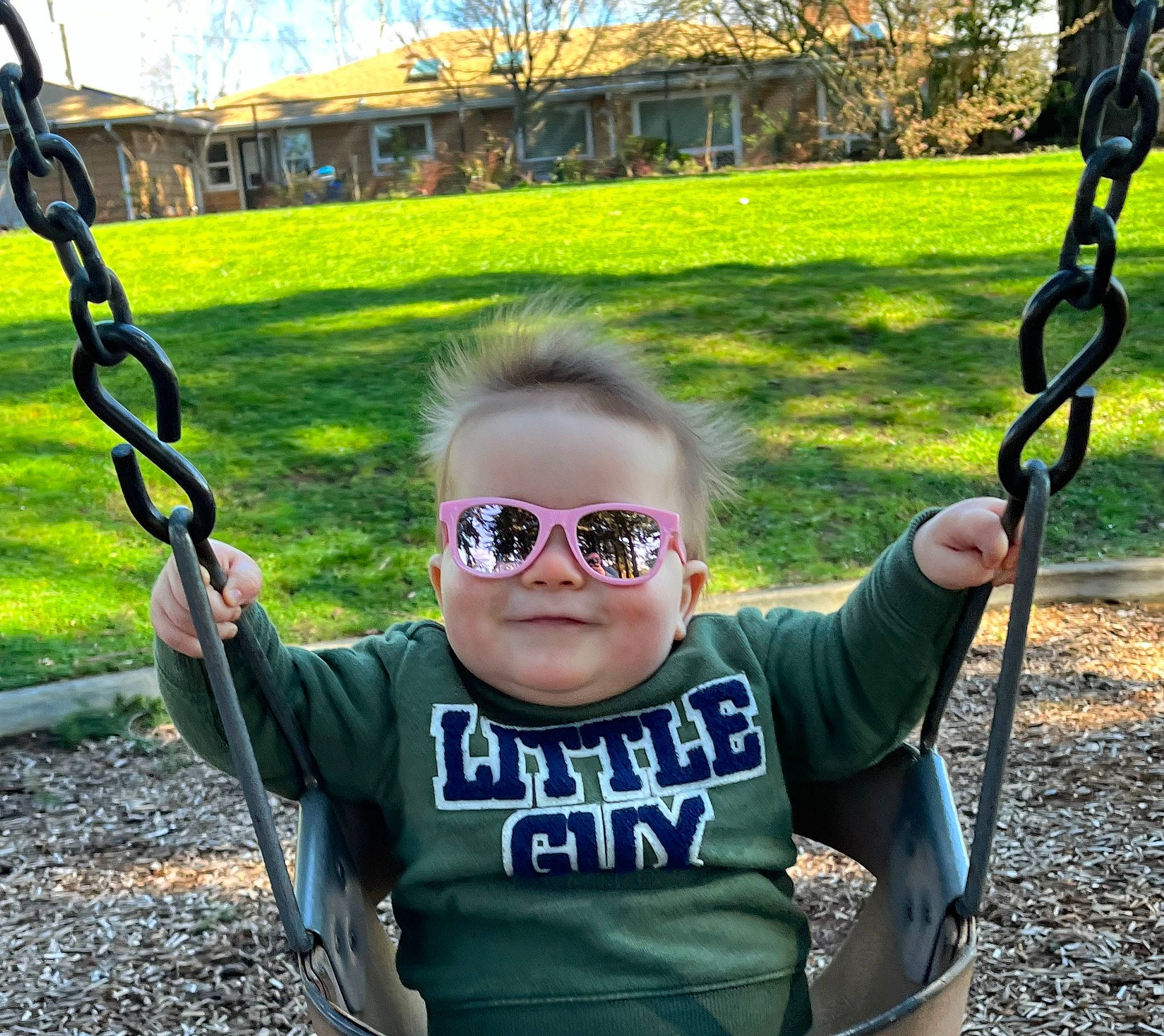 Milo is registered to the contest to win money with this photo: eyewear, facial_expression, glasses, grass, green, hand, happy, leaf, light, mammal, person, photograph, plant, sleeve, smile, standing, sunglasses, swing, tree, vertebrate