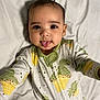 baby, child, tongue, onesie, dinosaur, ice_cream, bed, white_sheet, cute, infant, face, smile, happy, lying_down, pajamas, sleepwear, skin, head, expression, portrait