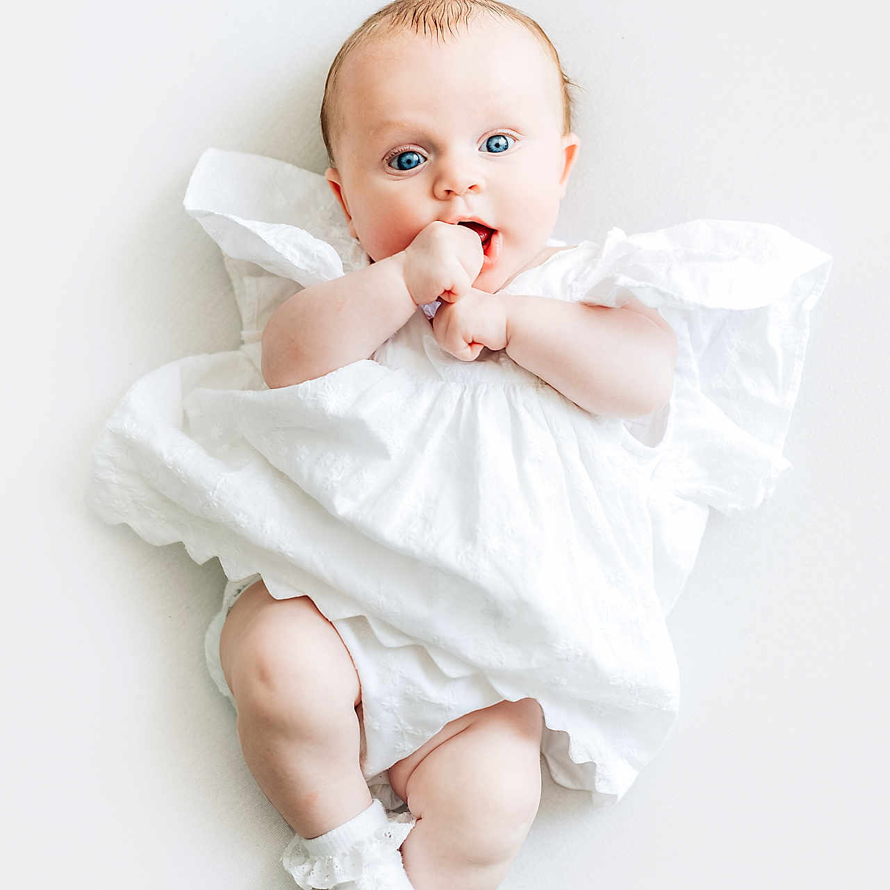 Valentina is registered to the contest to win money with this photo: baby, blue_eyes, child, close_up, curious, cute, expression, face, hands, infant, innocent, legs, lying_down, newborn, portrait, skin, socks, soft_lighting, studio_shot, white_dress