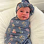 baby, newborn, swaddle, headband, floral_pattern, infant, cute, soft, blanket, lying_down, face, portrait, child, indoors, comfort, pink, blue, fabric, cushion, resting