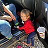 adult, barefoot, blue_pants, car, casual, child, cup, door, drink, flower, gravel, jeans, outdoor, person, red_shirt, smile, sneakers, sunlight, toddler, toy