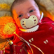 Jeanne participe au concours pour gagner de l'argent avec cette photo : baby, bows, child, closeup, cozy, cute, face, festive, glowing_lights, holiday, indoors, infant, pacifier, plush_blanket, portrait, red_clothing, soft_texture, star_ornament, string_lights, warm_lighting