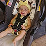 baby, child, smiling, yellow_headband, car_seat, safety_harness, infant, cute, happy, padded_seat, patterned_cushion, indoor, wooden_floor, clothing, person, headwear, baby_girl, seat_belt, closeup, portrait
