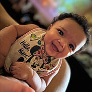 Isabel is registered to the contest to win money with this photo: baby, smile, curly_hair, bib, minnie_mouse, child, happy, portrait, indoor, skin, cute, infant, chubby, person, closeup, expression, apparel, colorful, soft_focus, hand