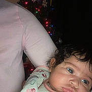 Solana is registered to the contest to win money with this photo: arm, baby, blue_eyes, child, christmas_lights, christmas_tree, clothing, curly_hair, cute, face, hand, holiday, indoor, infant, ornament, person, portrait, sleeve, soft_lighting, warmth