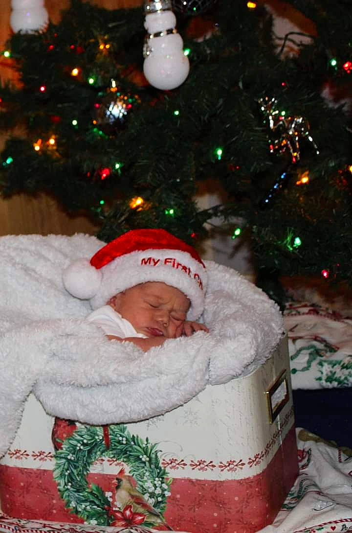 Lillie is registered to the contest to win money with this photo: baby, christmas, christmas_decoration, christmas_ornament, christmas_tree, event, face, facial_expression, green, happy, head, headwear, holiday, holiday_ornament, human_body, lap, light, person, standing, toddler