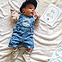 baby, blanket, card, casual_clothing, cute, denim_overalls, face, footwear, hand, hat, indoor, infant, lying_down, milestone_card, portrait, relaxed, small_shoes, socks, soft_texture, young_child