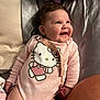 baby, smiling, pink_onesie, hello_kitty, pacifier_clip, chubby_cheeks, indoor, bed, pillow, blanket, cute, happy, child, infant, face, person, clothing, lying_down, soft_lighting, head