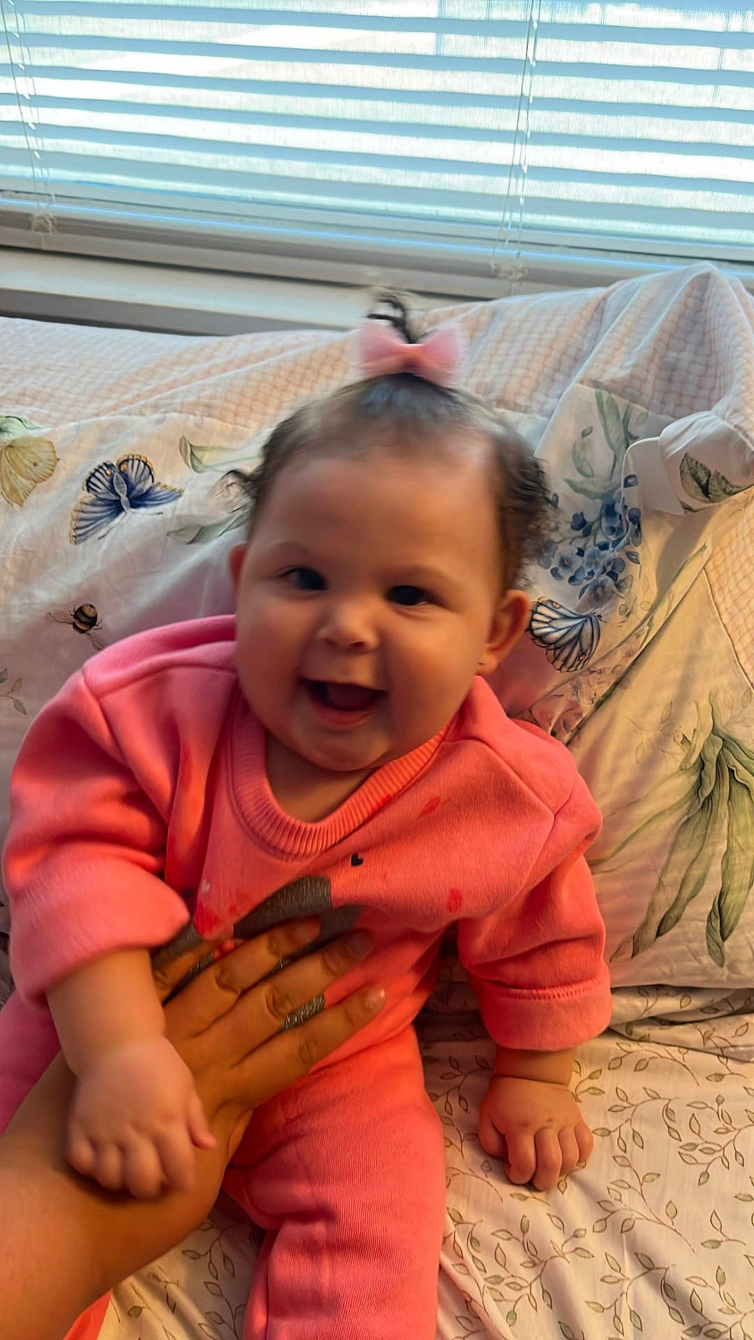 Yma Isabell is registered to the contest to win money with this photo: baby, pink_outfit, bow, hand, bedspread, floral_pattern, window_blinds, smiling, indoors, child, person, cute, happy, sitting, portrait, infant, clothing, skin, fingers, face