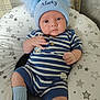 baby, infant, hat, pom_poms, blue_hat, striped_clothing, peter_rabbit, socks, white_shoes, cushion, star_pattern, plush_cushion, seated, indoors, cute, child, portrait, baby_clothes, knitwear, soft_furniture