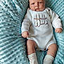 baby, infant, child, white_knit_outfit, hello_world_text, socks, blue_blanket, soft_texture, plush, cute, portrait, lying_down, expression, face, skin, newborn, cozy, comfortable, indoors, person
