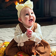 Riley is registered to the contest to win money with this photo: autumn, baby, bow, celebration, child, clothing, cozy, cute, decorations, dress, fall, fireplace, happy, indoor, leaves, person, portrait, sitting, smiling, warm