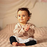 Charlie a rejoint le concours — aidez-le/la à gagner de superbes lots ! baby, bed, black_pants, blanket, child, clapping, cozy, curly_hair, cute, expression, face, indoors, infant, long_sleeve_shirt, person, sitting, smiling, soft_lighting, warm_colors, young