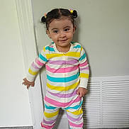 Fatima is registered to the contest to win money with this photo: child, toddler, girl, portrait, standing, smiling, pigtails, hair_bows, striped_clothing, rainbow_colors, onesie, pajamas, indoors, door, vent, carpet, home, full_body, happy, fashion