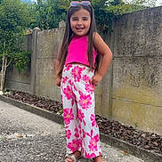 Taïsiana a rejoint le concours — aidez-le/la à gagner de superbes lots ! child, girl, smiling, outdoor, pants, pink, top, sunglasses, concrete_wall, plants, greenery, sidewalk, feet, sandals, long_hair, happy, daylight, casual_clothing, standing, nature