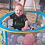 baby, child, ball_pit, toys, indoor, floor, blanket, chair, furniture, smiling, happy, person, clothing, sport_jersey, balls, playtime, cute, infant, home, colorful