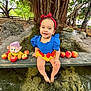 toddler, child, smiling, blue_dress, red_headband, apples, plush_toy, water, tree_roots, outdoor, nature, bench, park, happy, feet_in_water, costume, playful, cute, daylight, greenery