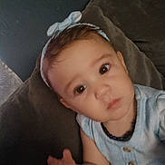 Aryya is registered to the contest to win money with this photo: baby, child, infant, portrait, face, eyes, gazing, sitting, cushion, indoor, close_up, bow, headband, striped_clothing, blue_outfit, hand, arm, cozy, home, photograph