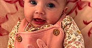 Lillith is registered to the contest to win money with this photo: baby, infant, face, expression, pink_overall, bunny_design, floral_shirt, blanket, cozy, indoor, brick_wall, cute, child, portrait, smile, wide_eyes, young_child, person, apparel, soft_texture