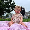 Lillith is registered to the contest to win money with this photo: baby, child, infant, smiling, sitting, outdoor, grass, blanket, pink_blanket, floral_clothing, onesie, portrait, face, eyes, hair, suburban, houses, trees, american_flag, daylight
