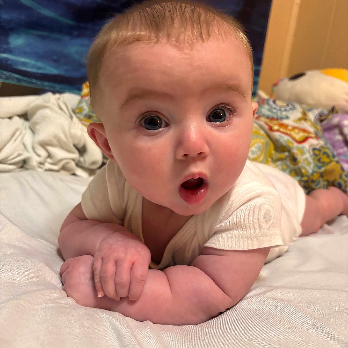 Lillith joined the competition — help win amazing prizes! baby, infant, child, tummy, surprised_expression, wide_eyes, skin, hand, white_clothing, blanket, bed, soft_surface, indoors, cute, portrait, face, head, resting, colorful, expression