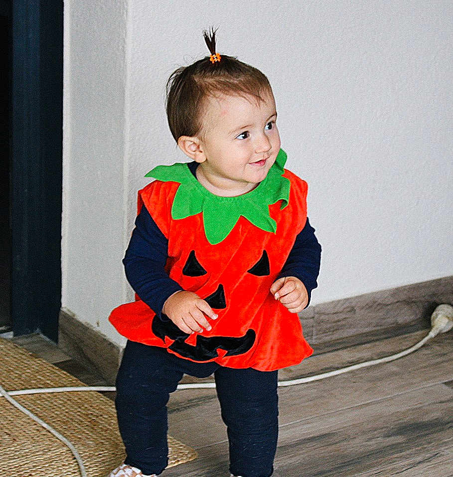 Liv a rejoint le concours — aidez-le/la à gagner de superbes lots ! toddler, child, pumpkin_costume, orange, green, black, smile, indoor, floor, wooden_floor, hair_tie, standing, cute, costume, holiday, happy, person, clothing, playful, young_child