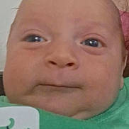 Jakob is registered to the contest to win money with this photo: baby, closeup, face, infant, green_clothing, dinosaur_print, child, portrait, skin, head, expression, young, person, newborn, baby_face, cute, indoors, human, soft_lighting, serious