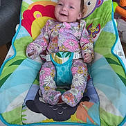 Amelie joined the competition — help win amazing prizes! baby, infant, smiling, floral_clothing, baby_bouncer, colorful, indoor, wooden_floor, toy, playful, happy, child, seat, fabric, pattern, cute, person, young_child, comfort, portrait