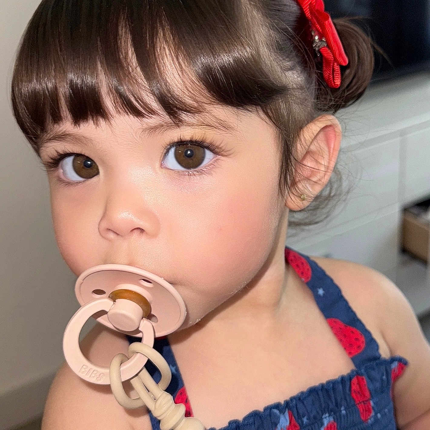 Georgina joined the competition — help win amazing prizes! accessory, baby, blue_dress, brown_eyes, child, close_up, clothing, curious, cute, expression, face, hair, indoor, pacifier, person, portrait, red_bow, skin, toddler, young_child