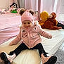 bedroom, boots, carpet, child, cozy, curtains, indoor, mattress, mittens, monkey_toy, pink_coat, pink_hat, playful, plush_toys, sitting, smiling, soft_lighting, toddler, window, yellow_toy