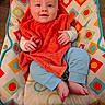 baby, child, smile, orange_towel, blue_pants, barefoot, cushion, patterned_fabric, indoor, happy, seated, infant, colorful, face, hand, foot, wooden_floor, cute, portrait, cozy