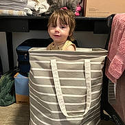 Axel is registered to the contest to win money with this photo: toddler, child, laundry_basket, kitten, cat, striped, indoor, floor, shelf, boxes, towels, clothing, pink_towel, curious, playful, pet, young_child, expression, storage, household