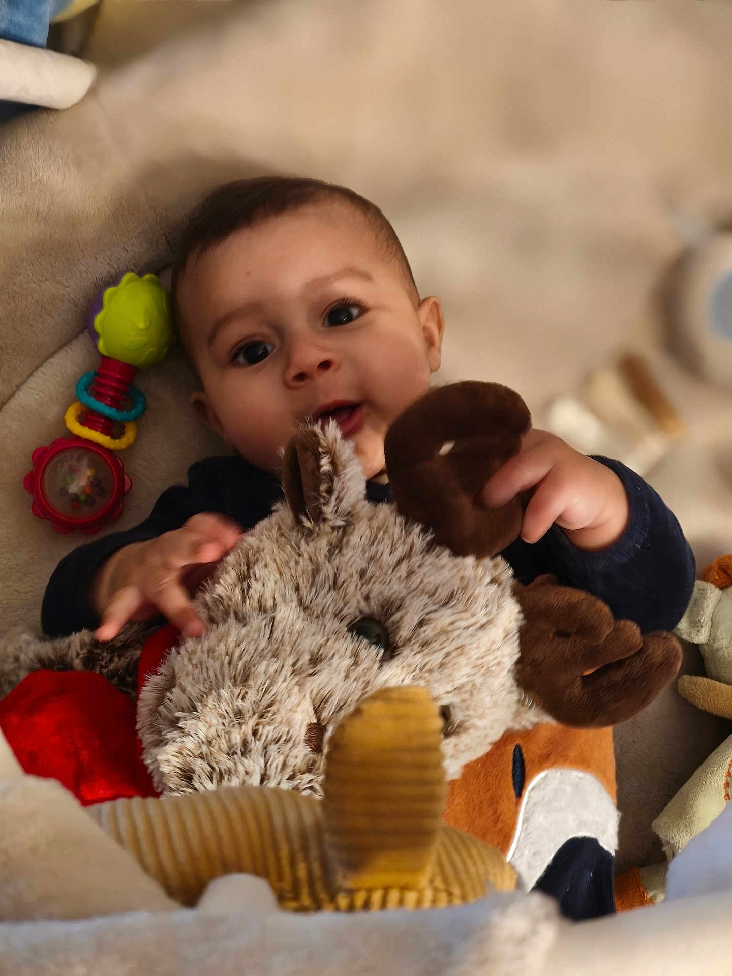 Kinsley a rejoint le concours — aidez-le/la à gagner de superbes lots ! baby, plush_toy, reindeer, child, soft_surface, colorful_toy, hand, face, smile, indoor, cute, furniture, cushion, cozy, warm, toy, infant, comfort, playing, young_child