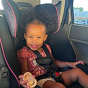 Love is registered to the contest to win money with this photo: toddler, child, car_seat, curly_hair, smiling, pacifier, seatbelt, car_interior, sunlight, happy, cute, safety, portrait, young_child, black_hair, clothing, window, daylight, person, seat