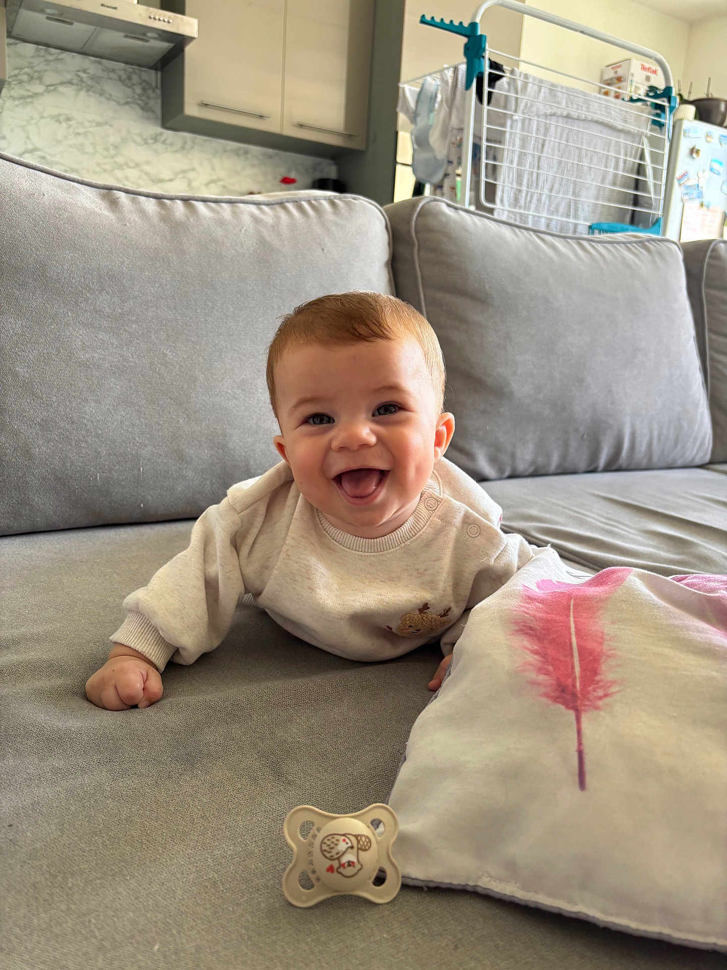 Gabriel a rejoint le concours — aidez-le/la à gagner de superbes lots ! baby, smiling, couch, pillow, pacifier, indoor, living_room, happy, face, child, clothing, furniture, dimples, head, person, infant, sleeve, blanket, kitchen, drying_rack