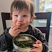 Brandon joined the competition — help win amazing prizes! toddler, child, baby, smiling, eating, food, bowl, vegetables, green_beans, snack, high_chair, indoor, portrait, face, hands, brown_hair, black_shirt, dining, window, happy