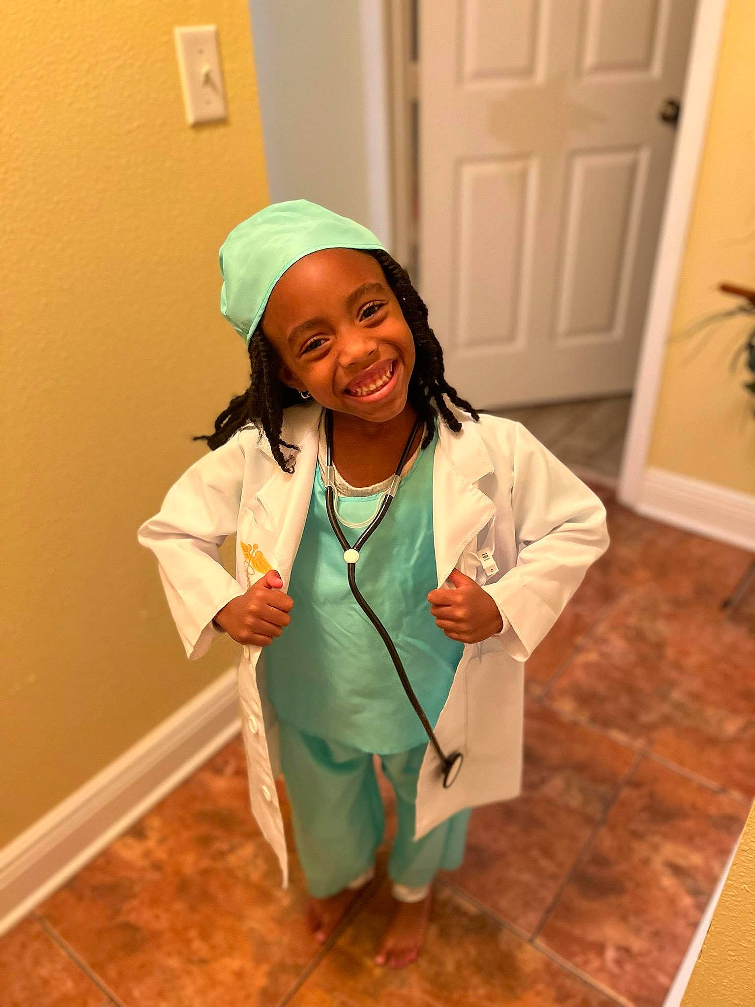 Jeveah is registered to the contest to win money with this photo: child, clothing, costume, door, fashion_design, flooring, flowerpot, hardwood, headwear, health_care_provider, houseplant, job, joy, medical, nurse, person, physician, plant, room, service