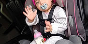 Victoria is registered to the contest to win money with this photo: baby, beanie, bottle, car_interior, car_seat, child, cup_holder, footwear, gray_clothing, hand_raised, hat, houses, pacifier, person, seat, seatbelt, sneakers, toddler, vehicle, window