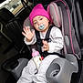 toddler, child, car_seat, pacifier, bottle, hat, beanie, gray_clothing, car_interior, seatbelt, cup_holder, window, houses, hand_raised, footwear, sneakers, baby, person, seat, vehicle