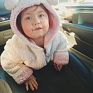 Victoria is registered to the contest to win money with this photo: child, toddler, hooded_jacket, fluffy_clothing, pink, white, car_interior, seat, hand, face, portrait, curious, cute, casual, indoor, warm_clothing, young_child, baby, person, cozy