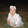 child, toddler, girl, white_clothing, headband, flashlight, grass, night, outdoor, wire_fence, curious, crouching, polka_dot, long_sleeve, dress, headwear, person, young_child, looking_up, dark_background