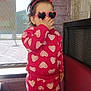 brick_wall, casual_wear, child, cozy, cute, fashion, fun, headband, heart_pattern, heart_sunglasses, indoor, person, playful, portrait, red_clothing, smiling, standing, toddler, window, young_child