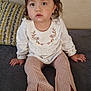 toddler, child, girl, bow, pink_bow, white_top, floral_embroidery, patterned_pants, barefoot, couch, gray_couch, indoor, portrait, sitting, curious, wide_eyes, hands, feet, face, hair