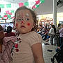 toddler, child, face_paint, clown_makeup, indoor, crowd, celebration, colorful_banners, people, adult, stroller, tile_floor, casual_clothing, event, family, portrait, curious, holding, shopping_mall, public_place