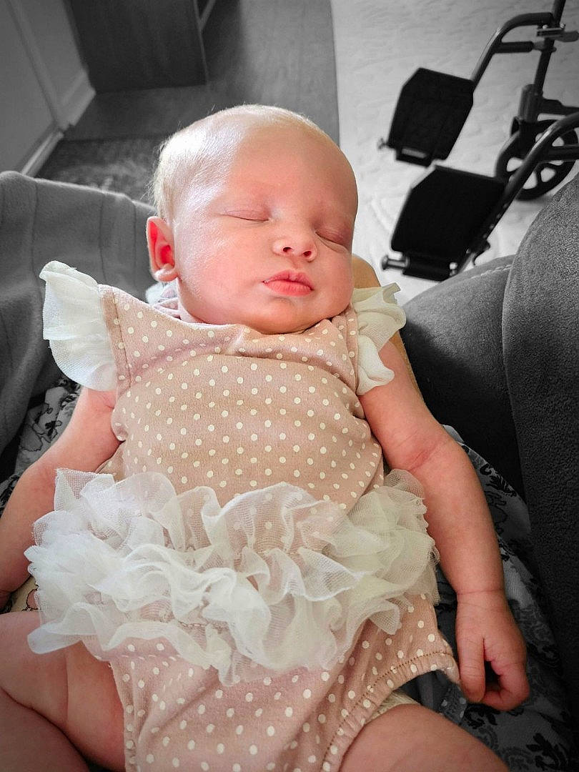 Gracelyn is registered to the contest to win money with this photo: abdomen, baby, baby_toddler_clothing, blond, child, comfort, embellishment, event, finger, hand, linens, pattern, peach, person, pink, product, sitting, skin, textile, thigh