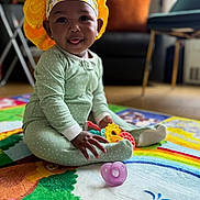 Nyla joined the competition — help win amazing prizes! baby, child, playmat, toys, onesie, headwear, yellow_bonnet, smiling, tongue_out, indoor, living_room, couch, colorful, floor, sitting, happy, cute, polka_dot, infant, playtime