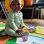 baby, child, playmat, toys, onesie, headwear, yellow_bonnet, smiling, tongue_out, indoor, living_room, couch, colorful, floor, sitting, happy, cute, polka_dot, infant, playtime