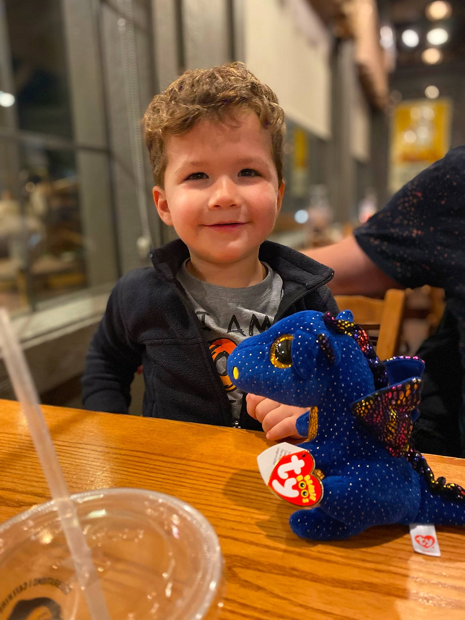 Patryk is registered to the contest to win money with this photo: arm, carmine, chair, child, desk, event, flooring, fun, hand, happy, joy, leisure, person, plate, smile, stuffed_toy, table, tableware, toddler, toy